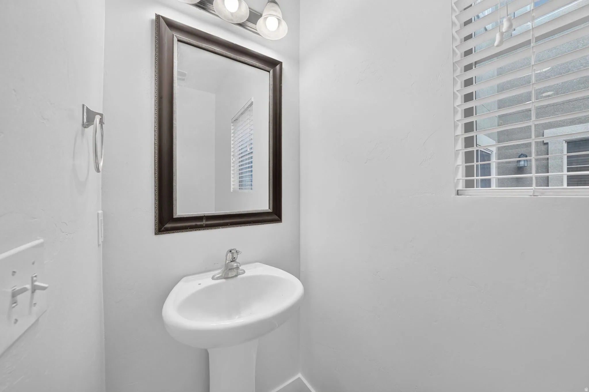 Pedestal sink with chrome faucet, framed mirror, and overhead vanity lighting