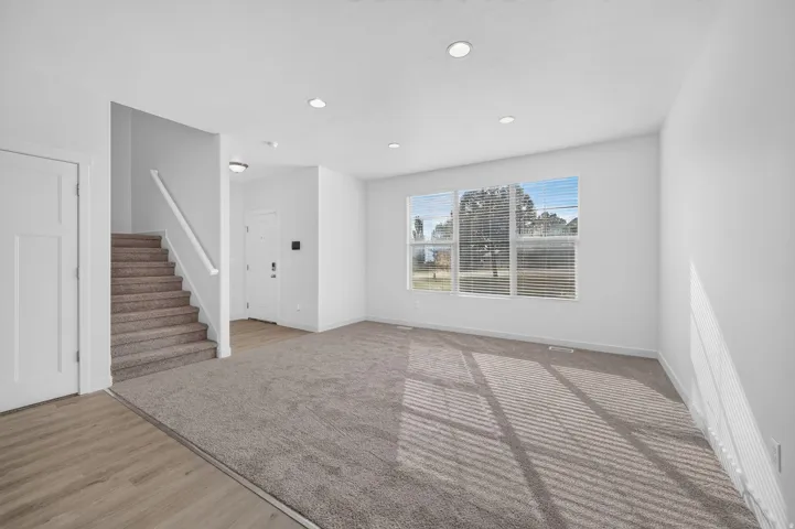 Spacious living area featuring neutral carpeting, recessed lighting, and large windows with blinds