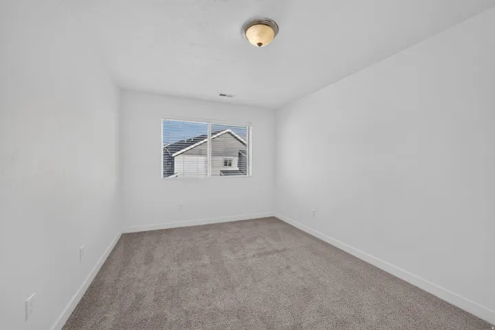 Carpeted room featuring white walls, a single window with blinds, and a ceiling-mounted light fixture
