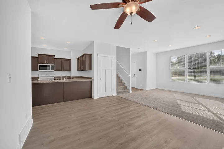 Open-concept living space with wood-finish flooring transitioning to carpet, recessed lighting, and a ceiling fan