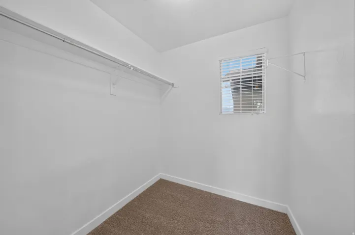 Well-lit closet space featuring a built-in wire shelving system, a window with horizontal blinds, and neutral-toned carpeting