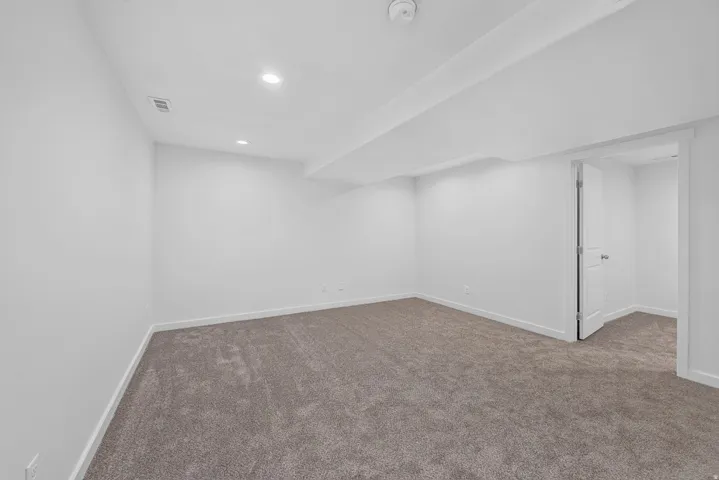 Spacious room featuring neutral carpeting, white painted walls, recessed lighting, and a white interior door
