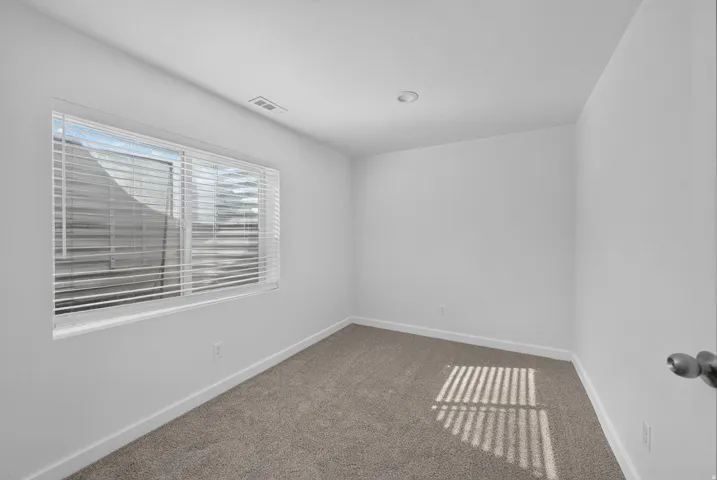 Room with light neutral carpeting, white walls, and a single window with horizontal blinds