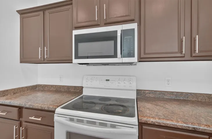 Kitchen featuring an electric range, over-the-range microwave, brown cabinetry, and patterned countertops
