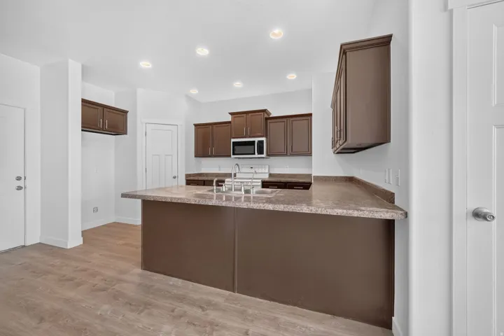 Kitchen featuring recessed lighting, a central island with an undermount sink, wood-finish flooring, and dark wood-finish cabinetry