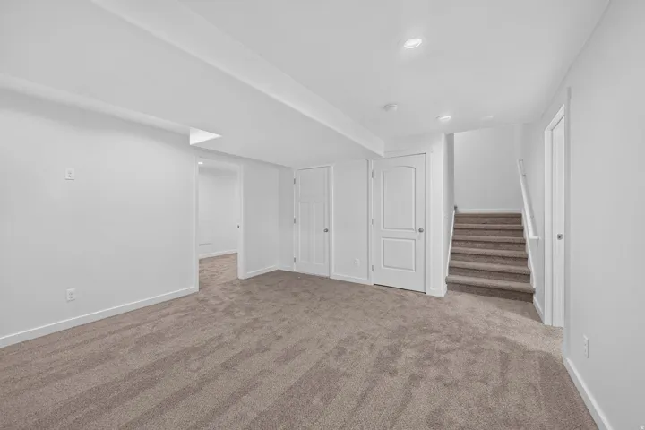 Spacious carpeted room featuring recessed lighting, white trim, solid white doors, and a carpeted staircase with a white handrail