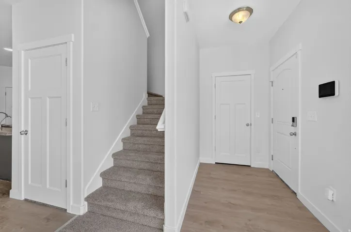 Foyer with light wood-finish flooring, white trim, and a carpeted staircase