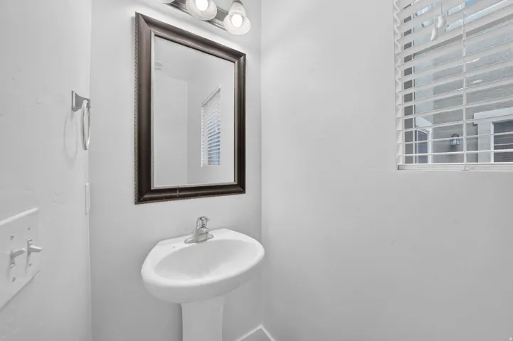 Pedestal sink with chrome faucet, framed mirror, and overhead vanity lighting
