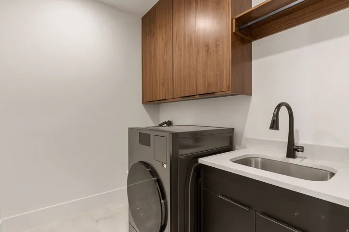 Utility area featuring a built-in sink with a matte black faucet, light-toned countertop, dark wood-finish lower cabinetry, and complementary wood-finish upper cabinetry