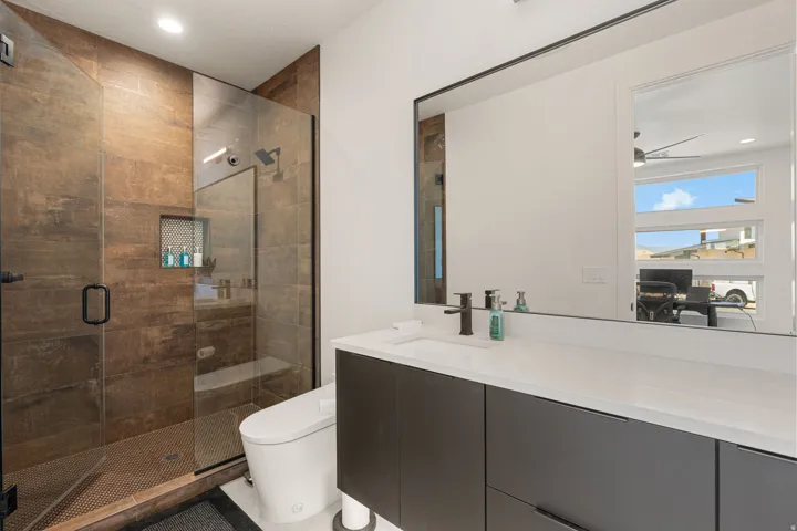 Modern bathroom featuring a frameless glass shower enclosure with a rain shower head, built-in shower niche, and rich brown tiled walls
