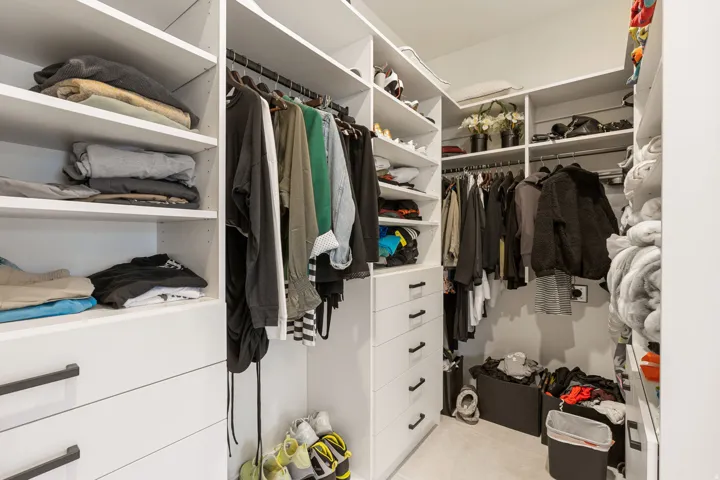 Custom closet system featuring extensive shelving, multiple hanging rods, built-in drawers with dark hardware, and bright interior lighting