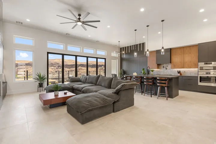 Open-concept living space featuring a modern kitchen with wood-finish and dark cabinetry, stainless steel built-in appliances, and a central island with pendant lighting