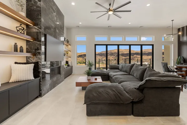 Spacious living area featuring light-toned flooring and a dark stone-clad accent wall with an integrated fireplace and television