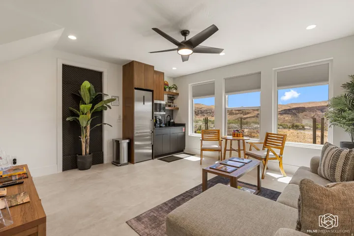 ADU integrated living area featuring a compact kitchen with wood-finish cabinetry and stainless steel appliances, three large windows, a ceiling fan, and recessed lighting