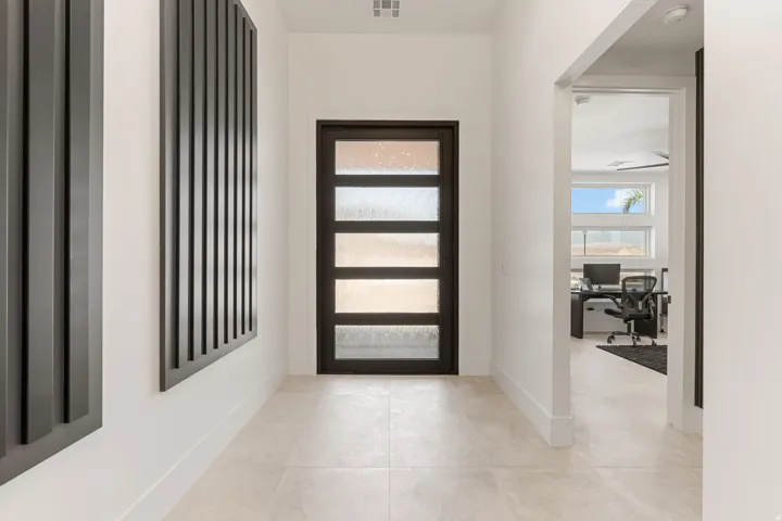Modern entryway featuring a dark-framed door with frosted glass panels, light-toned tile flooring, and clean white walls