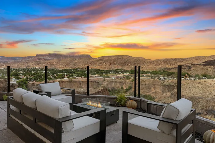 Outdoor patio featuring a built-in fire pit, glass railing, and a desert landscape backdrop with distant mesas, and Basalt Canyon and Virgin River below