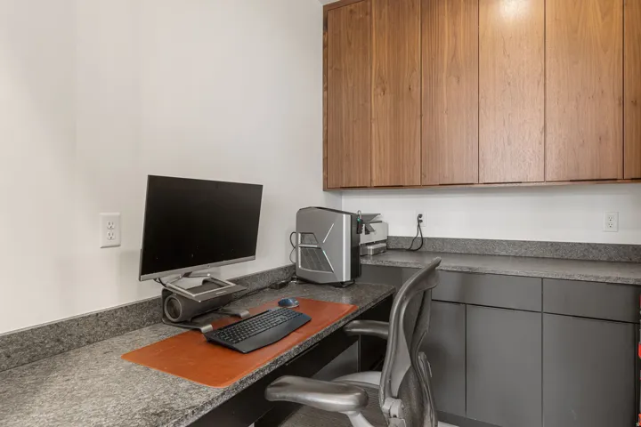Hidden pantry/office space featuring extensive built-in cabinetry, upper wood-finish storage, lower matte gray cabinets, and a durable stone-finish countertop