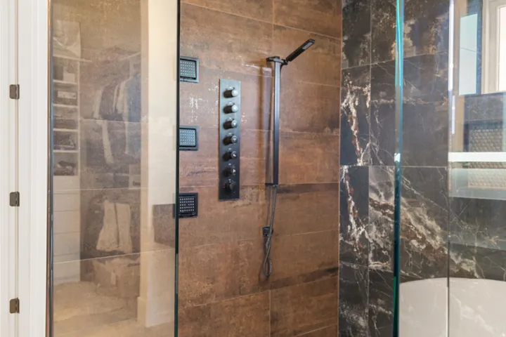 wet room shower featuring glass enclosure, large format brown-toned wall tiles, and a multi-setting shower system with dark bronze finish fixtures