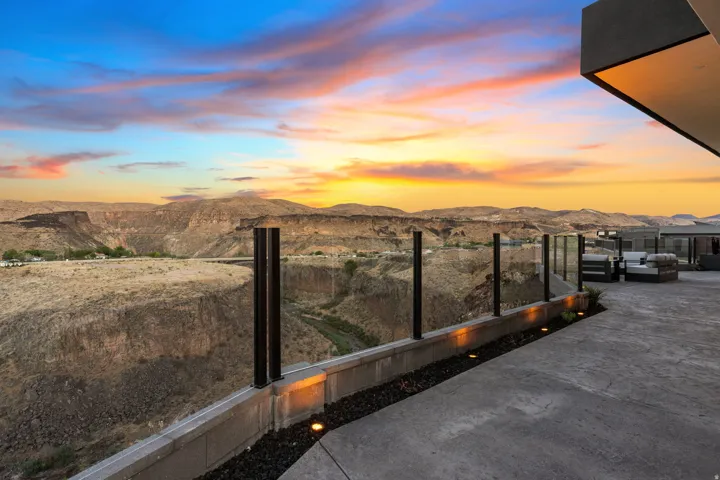Expansive outdoor patio with a glass railing system and integrated lighting, offering panoramic canyon and distant mountain scenery