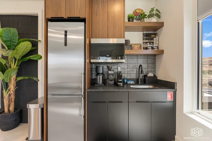 ADU kitchenette featuring wood-finish cabinetry, a stainless steel refrigerator, dark countertops, a rectangular sink with a matte black faucet, and gray tile backsplash