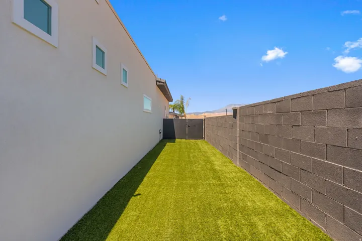 Side yard featuring artificial turf, a stucco exterior wall with multiple windows, and a block wall perimeter