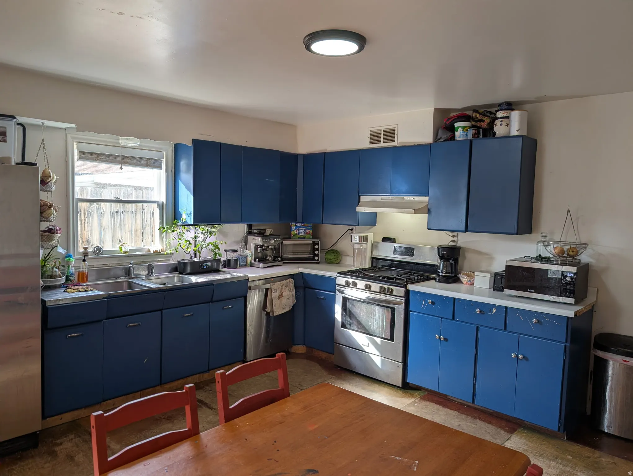 Kitchen with blue cabinetry, white countertops, stainless steel appliances, and a double basin sink