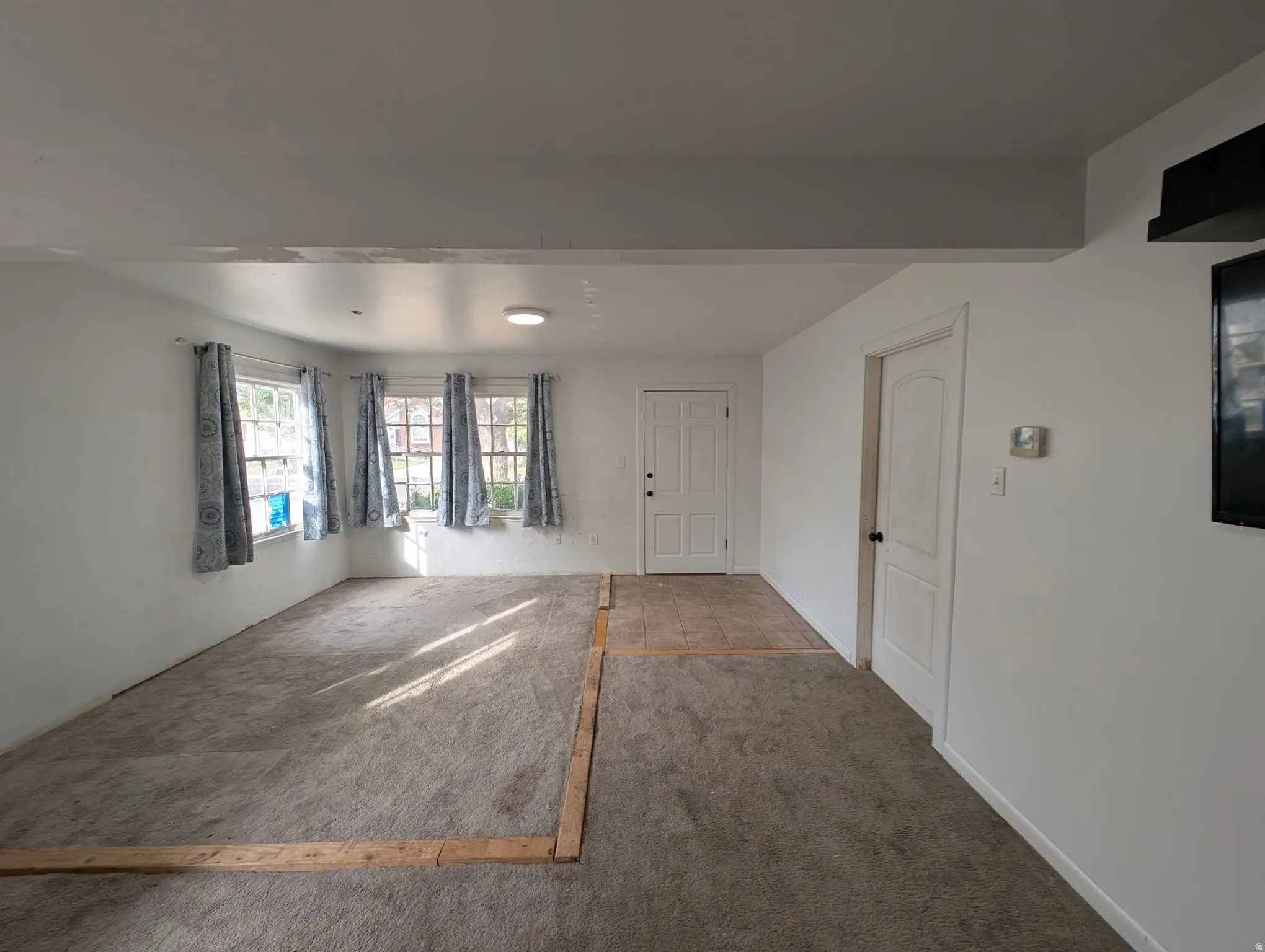 White painted walls, three double-hung windows, recessed ceiling lighting, and a white paneled door