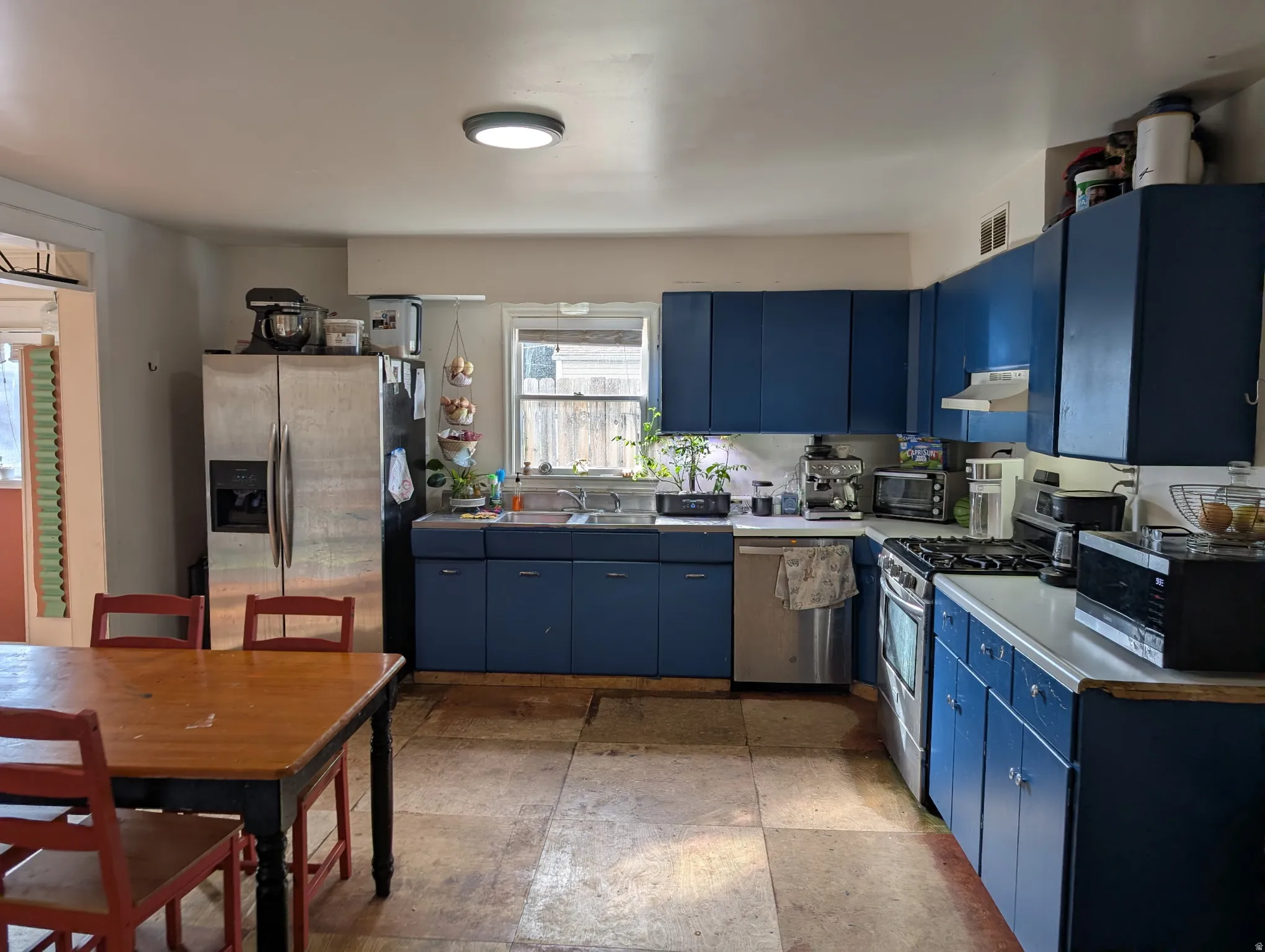 Kitchen featuring blue cabinetry, a stainless steel refrigerator, a gas range, and a window above the sink
