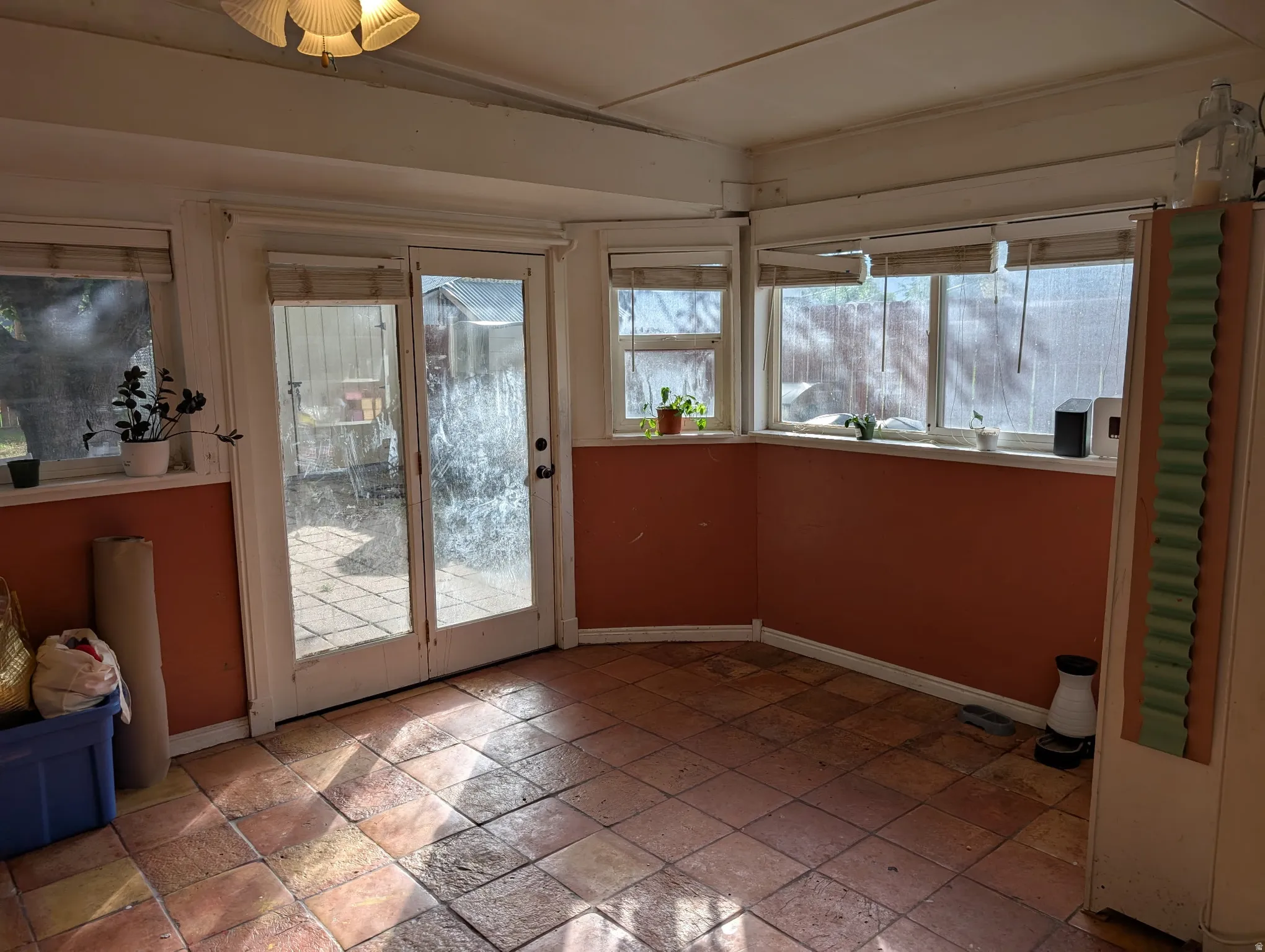 Terracotta tile flooring, multiple windows, double glass panel doors, and a ceiling-mounted light fixture