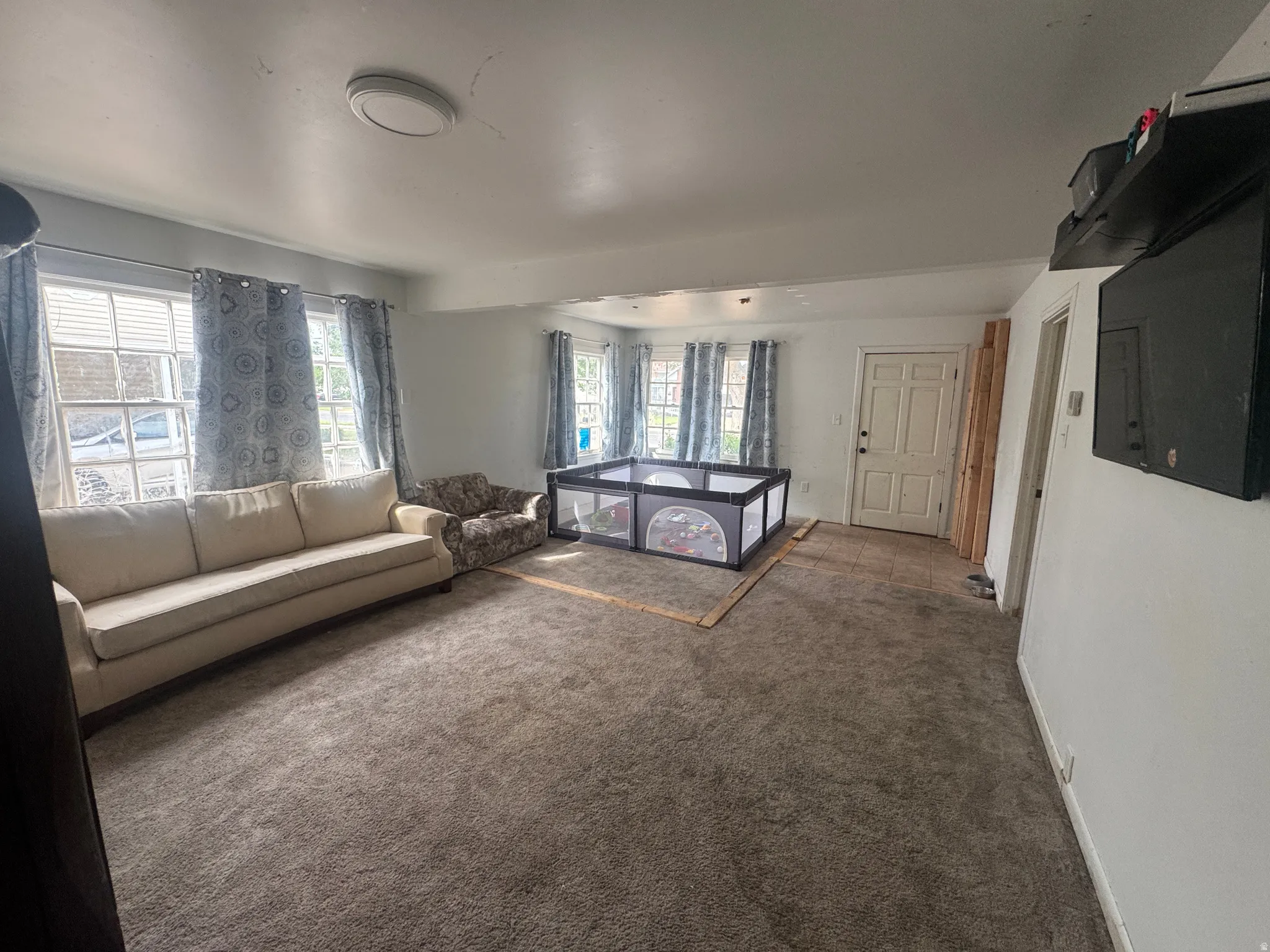 Spacious interior room with multiple windows, carpet flooring, and a paneled entry door