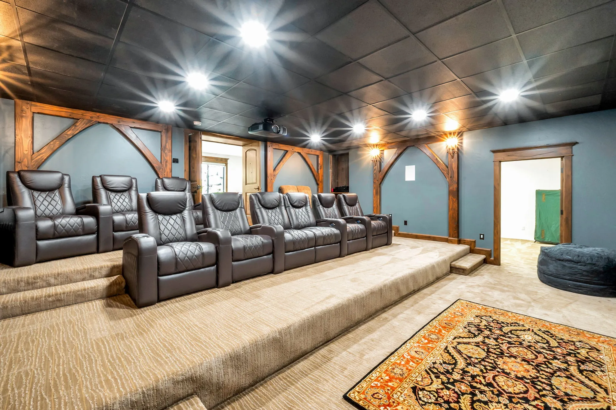 Dedicated home theater featuring tiered seating, wood-beamed wall accents, recessed lighting, and a ceiling-mounted projector