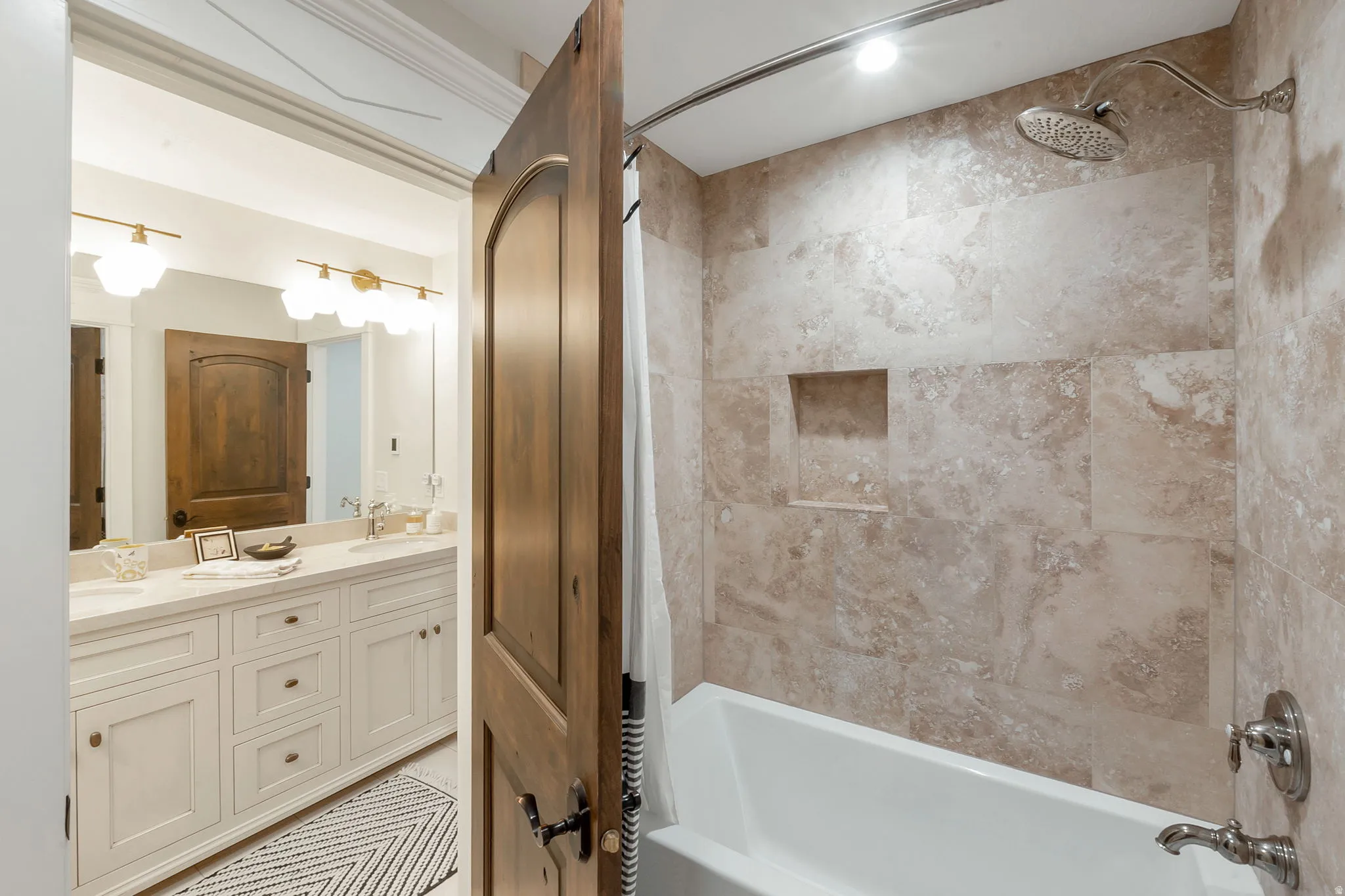 Bathtub with stone-tiled surround featuring a built-in shower niche, brushed nickel fixtures, and a rain showerhead