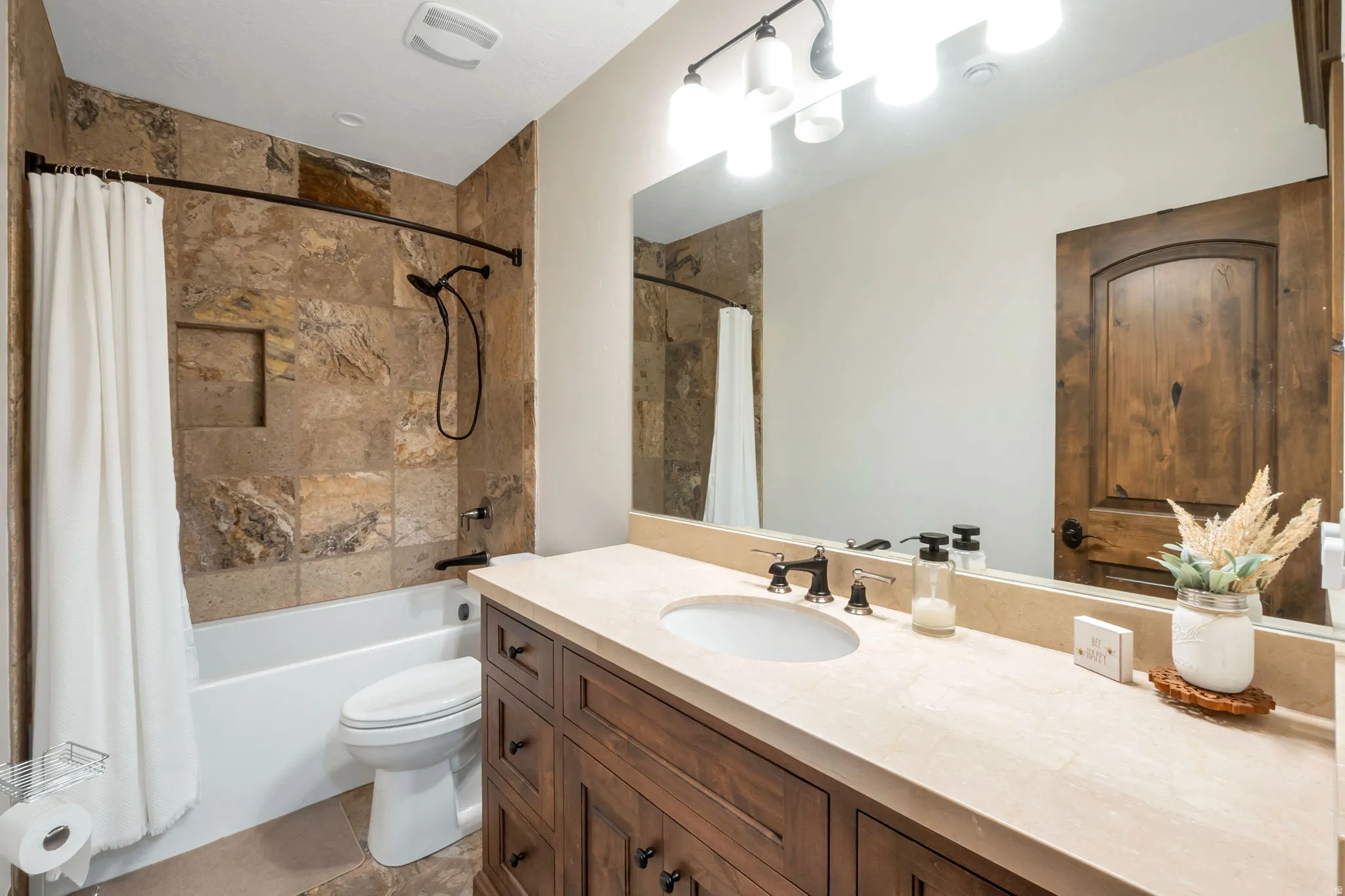 Bathroom featuring a stone-tiled shower surround with a built-in niche, a white tub, and a dark bronze shower fixture
