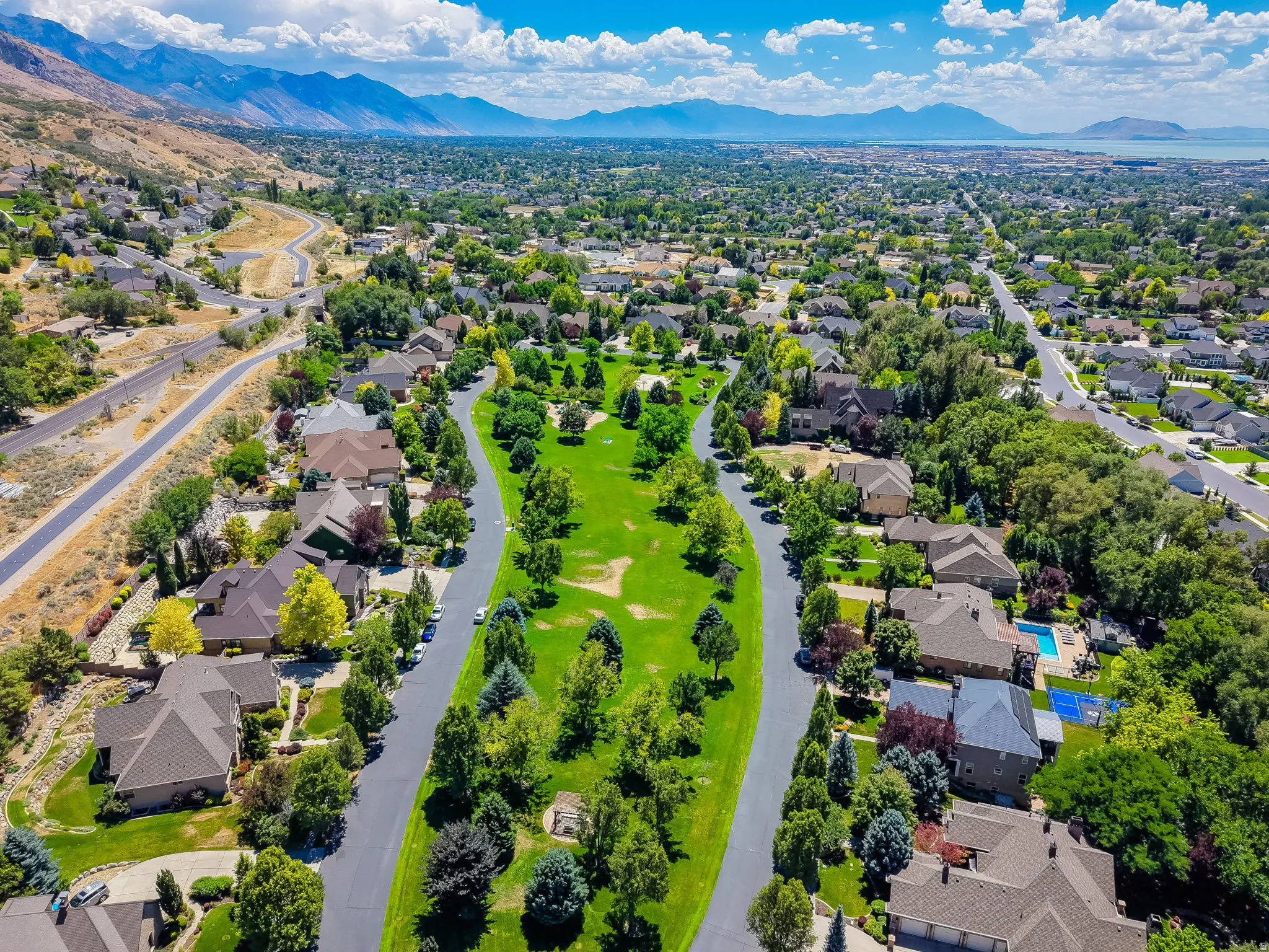 Expansive residential development featuring mature landscaping, paved roads, and distant mountain and water scenery