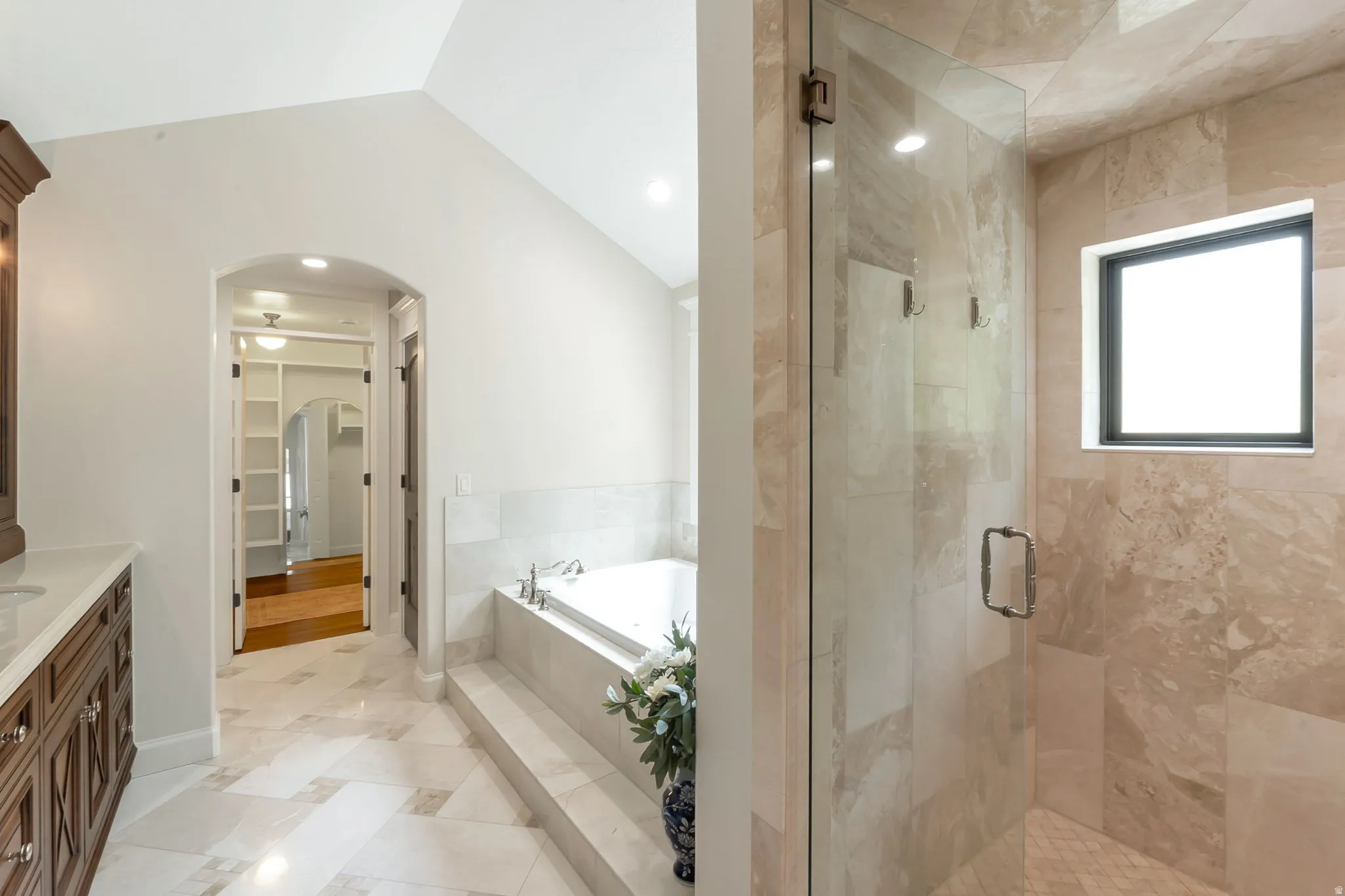 Spacious bathroom featuring a glass-enclosed shower, built-in soaking tub with tiled surround, vaulted ceiling, and patterned tile flooring
