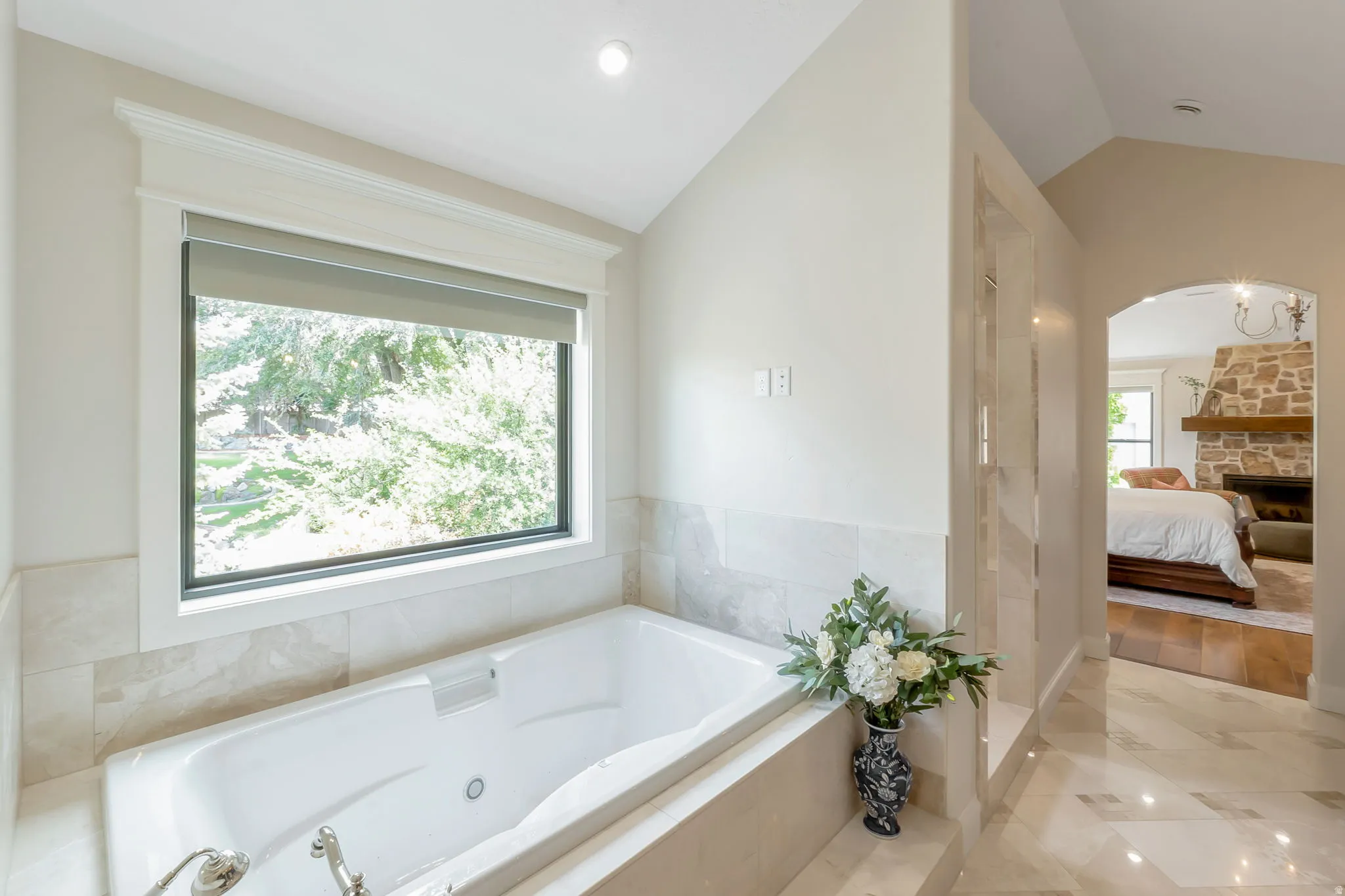 Soaking tub with jetted features set in a tiled surround, featuring a large window with roller shades