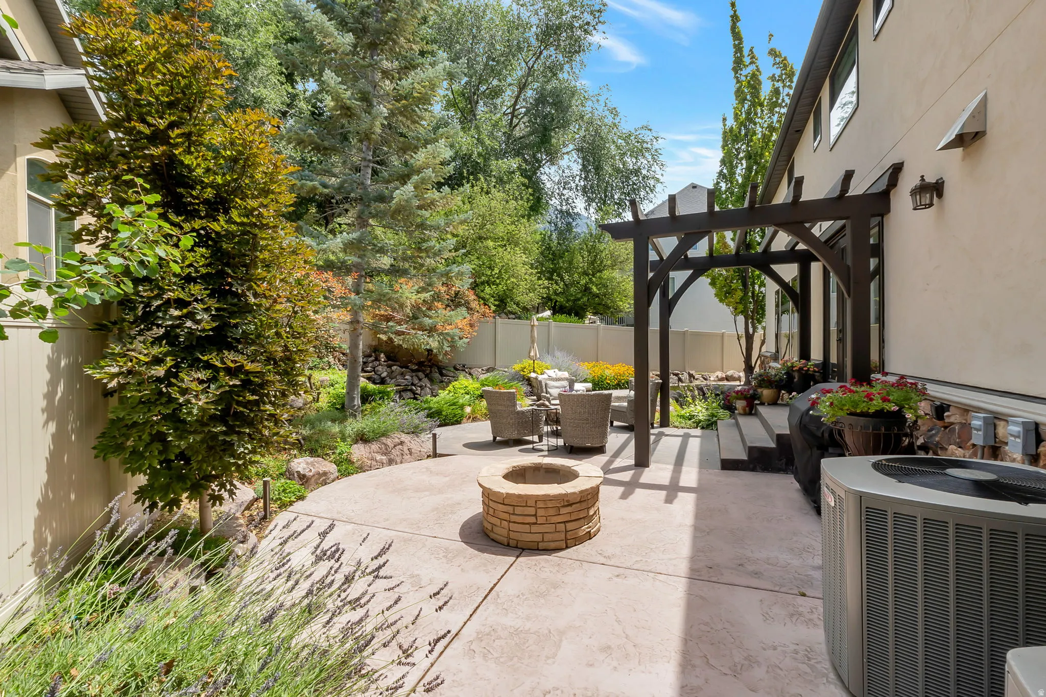 Stamped concrete patio featuring a built-in fire pit, a dark wood pergola, and diverse landscaping