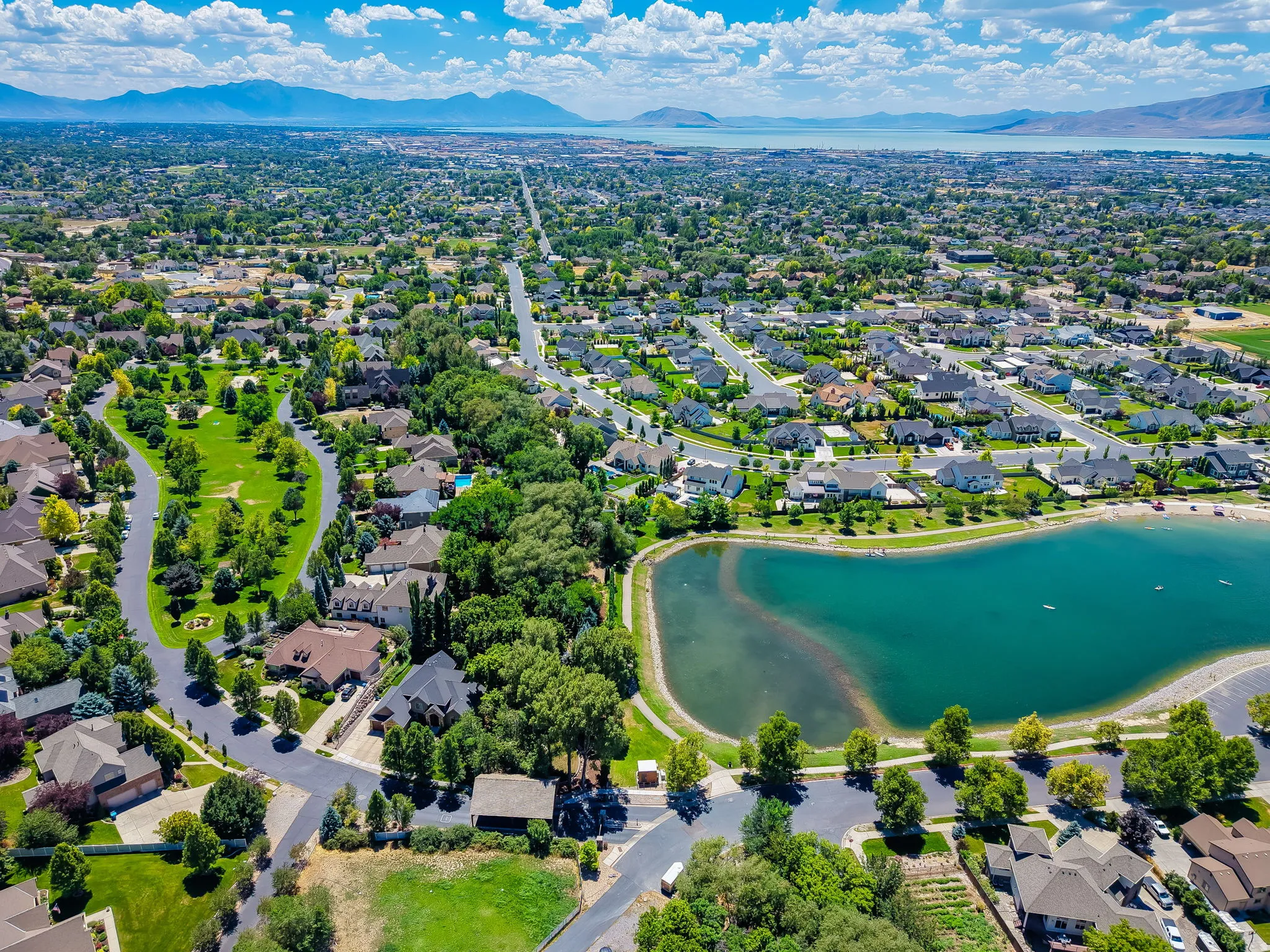 Expansive residential area featuring numerous single-family homes, mature trees, a large body of water, and distant mountains