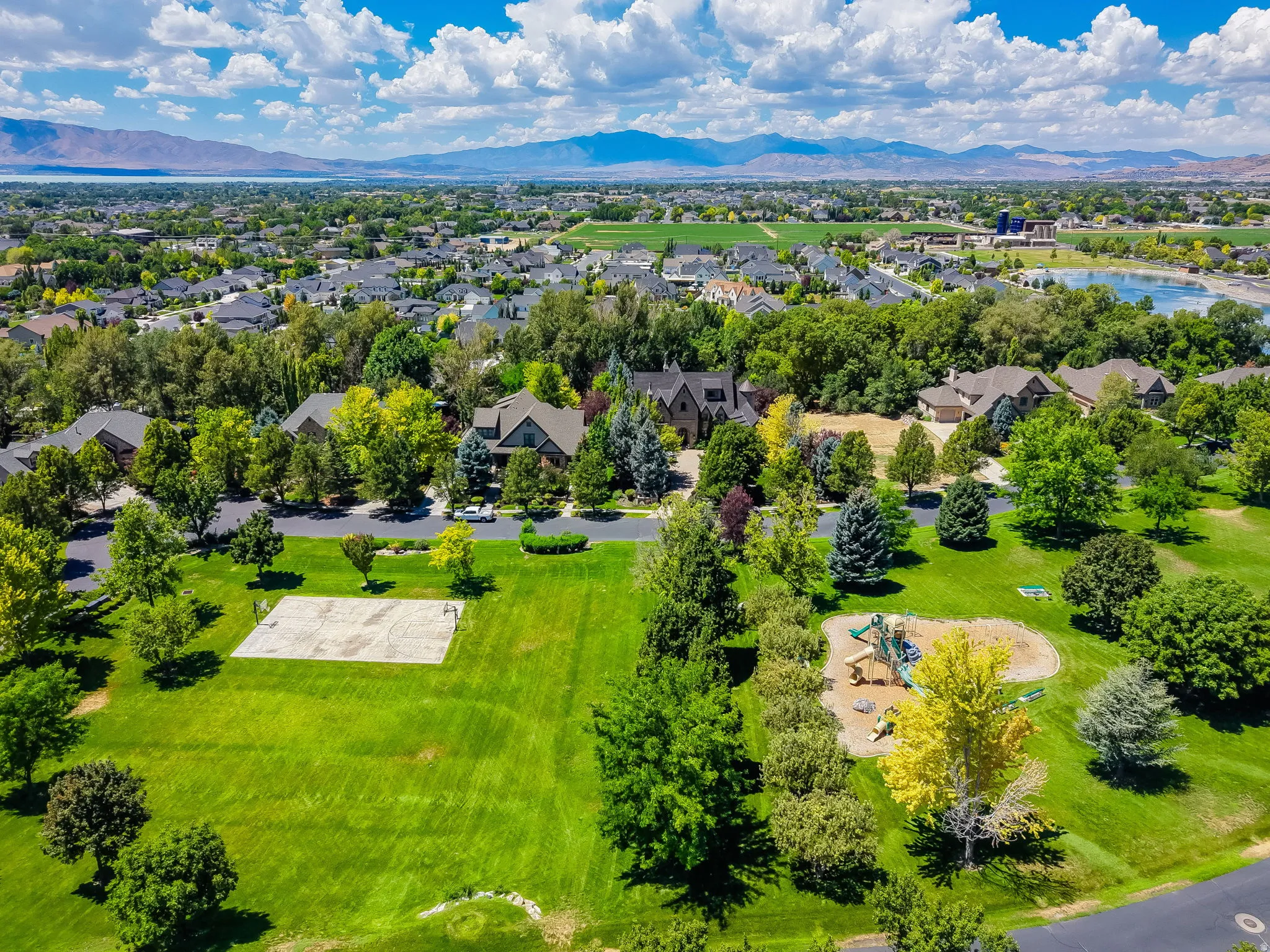 Expansive green space featuring a playground, sports court, mature trees, and surrounding residential properties