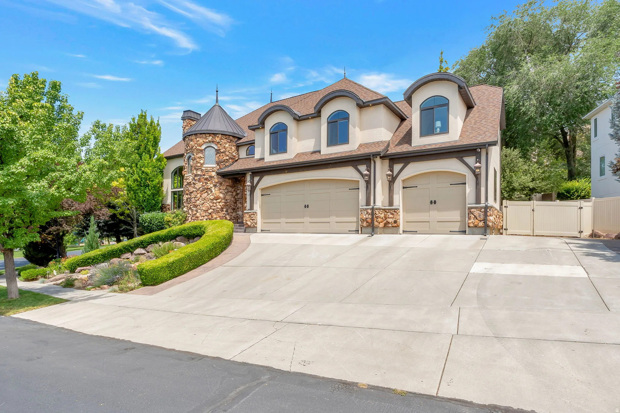 Stucco and stone exterior featuring a turret, arched dormer windows, and a multi-car garage with carriage-style doors