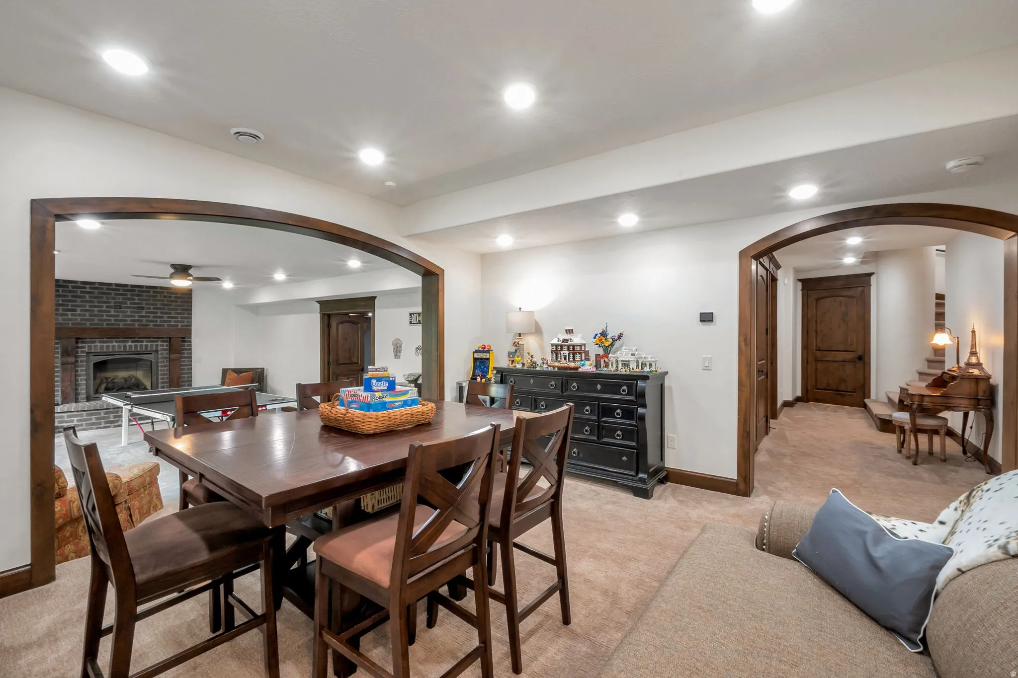 Recessed lighting illuminates an open-concept lower level featuring a carpeted entertainment area and a brick fireplace