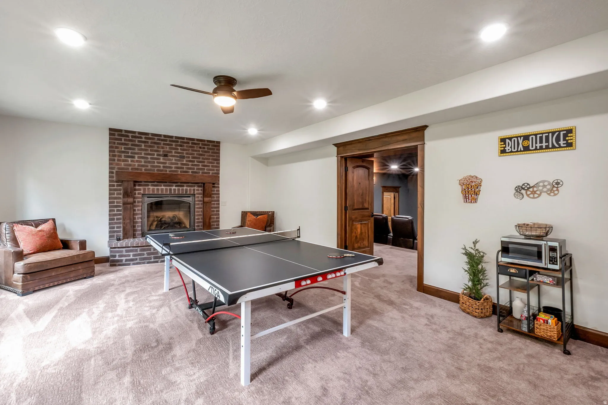 Spacious entertainment area featuring a brick fireplace with wood mantel, recessed lighting, ceiling fan, and carpet flooring