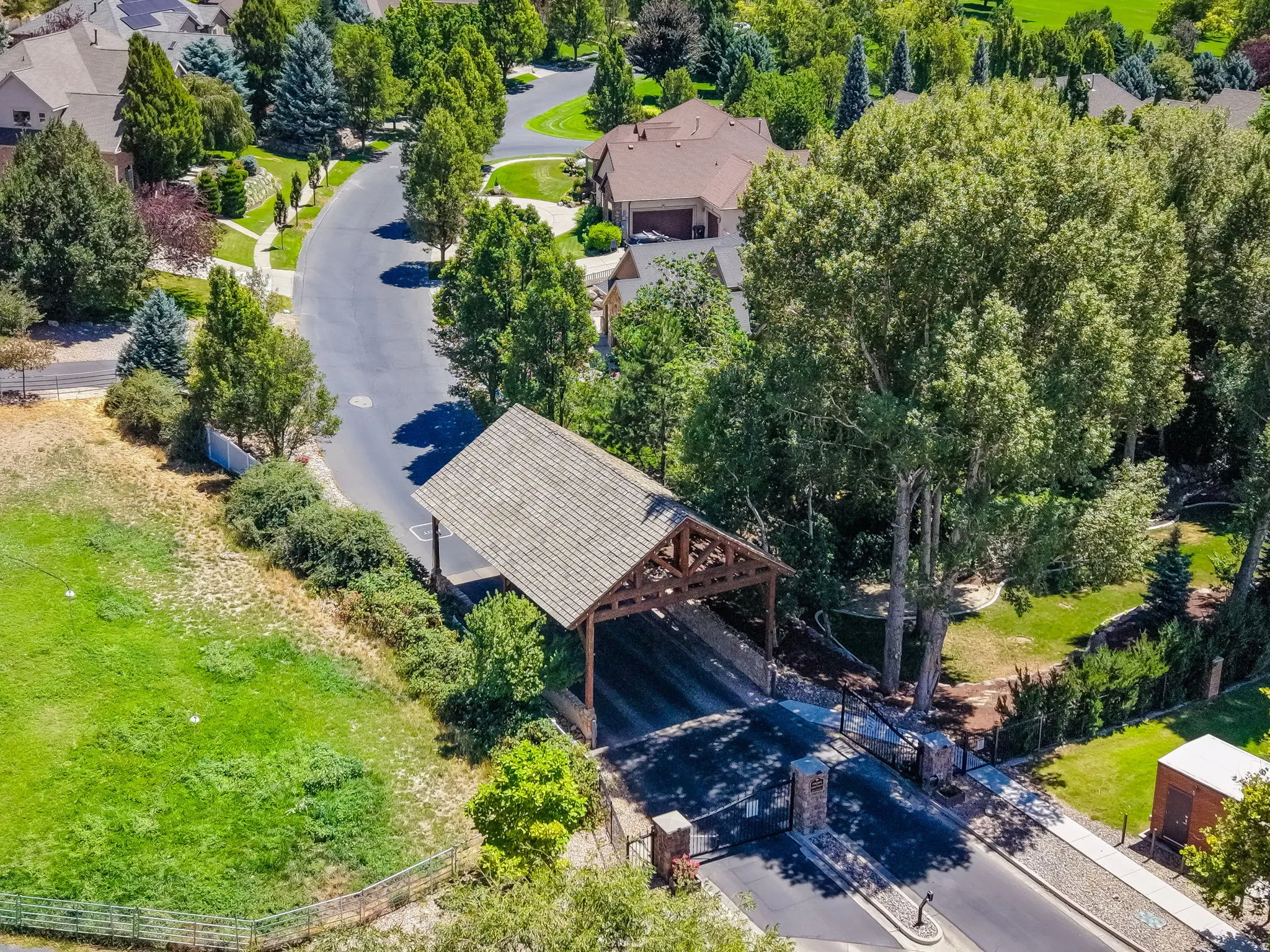 Entryway featuring a covered timber frame structure with a shingle roof, stone pillar gates, and a paved road