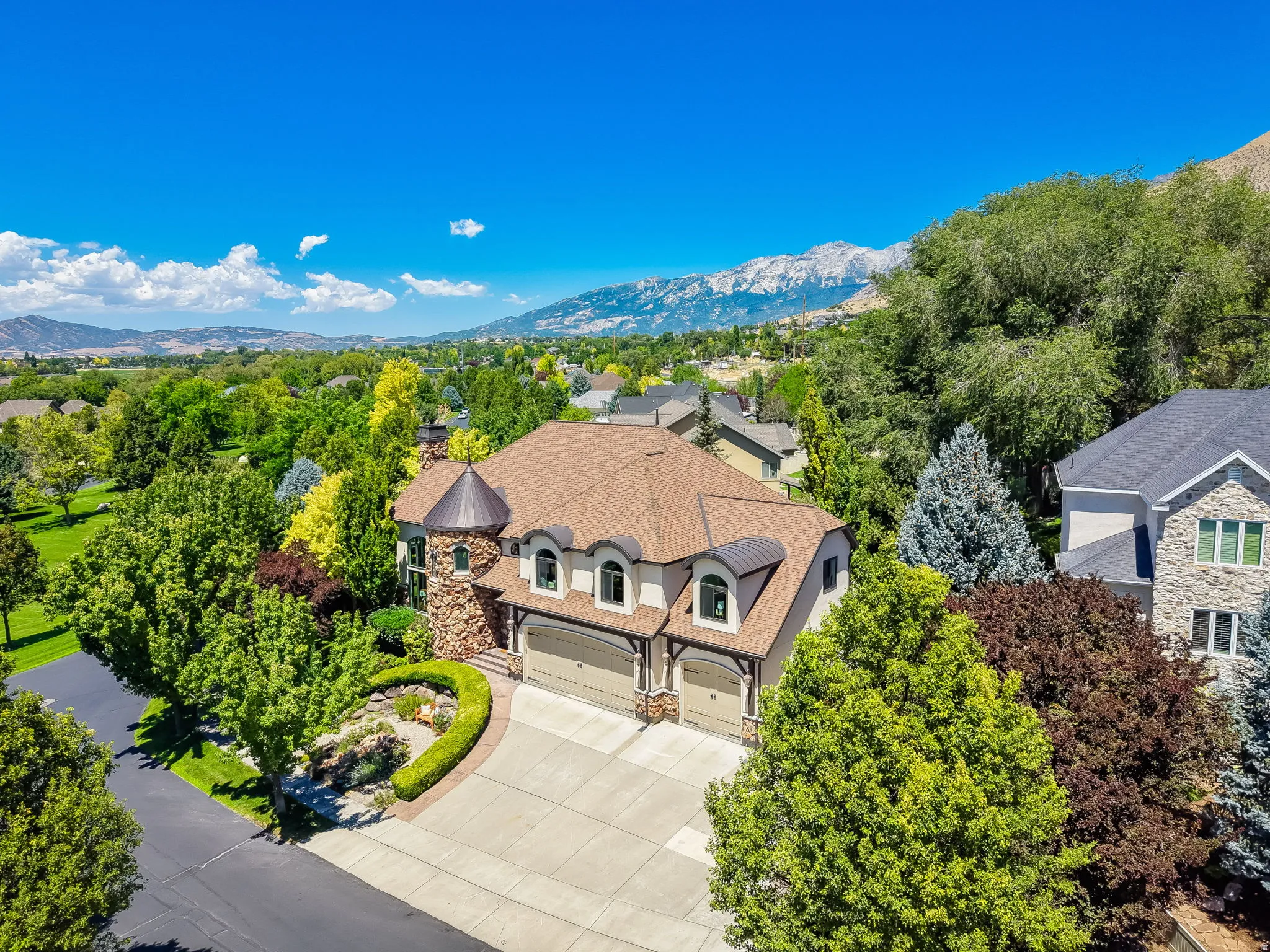 Stately residence featuring a stone-clad turret, arched windows, a multi-car garage, mature landscaping, and mountain scenery