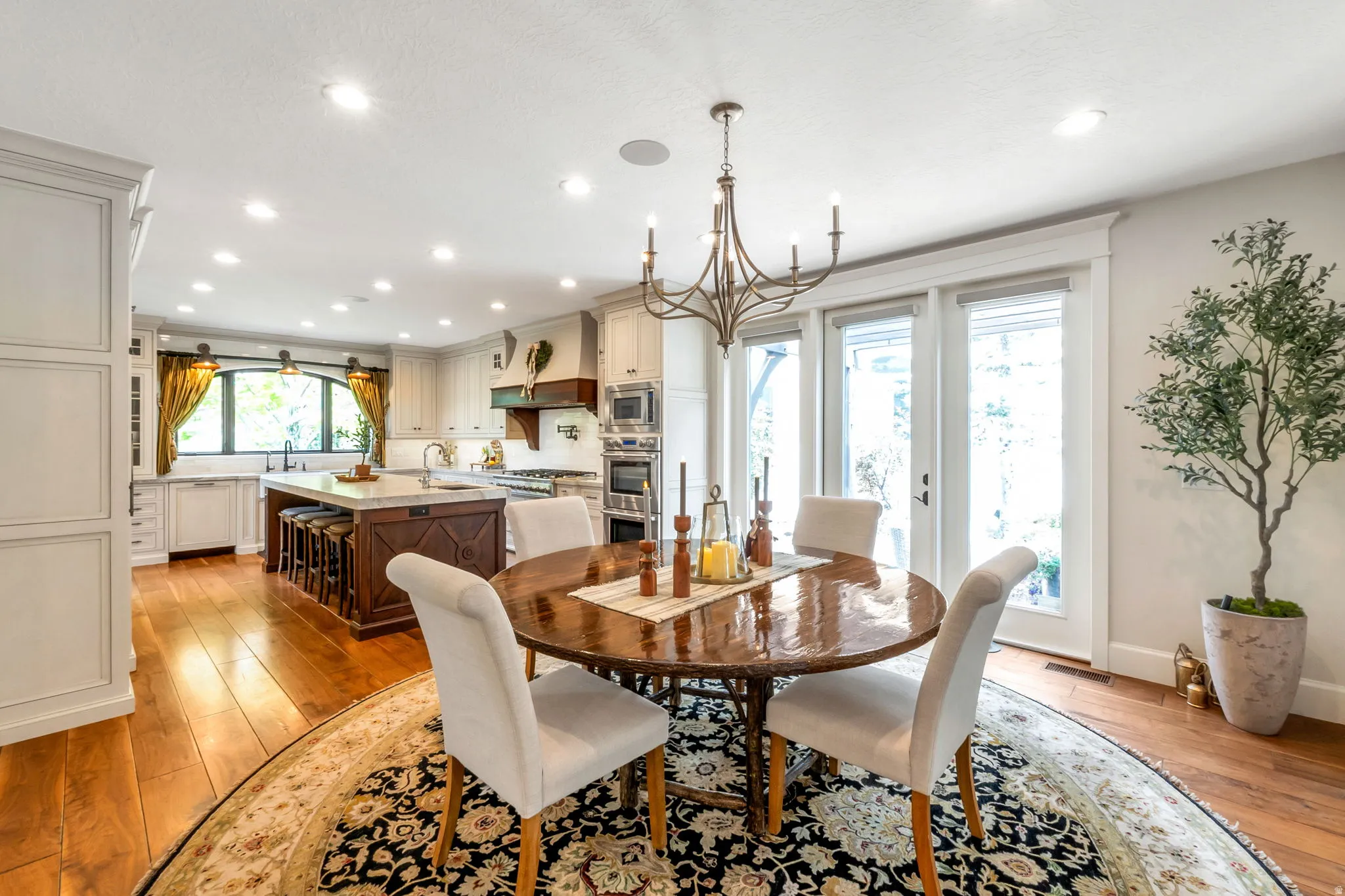 Spacious kitchen and dining area featuring hardwood flooring, a central island with seating, integrated appliances, and multiple glass-paned doors