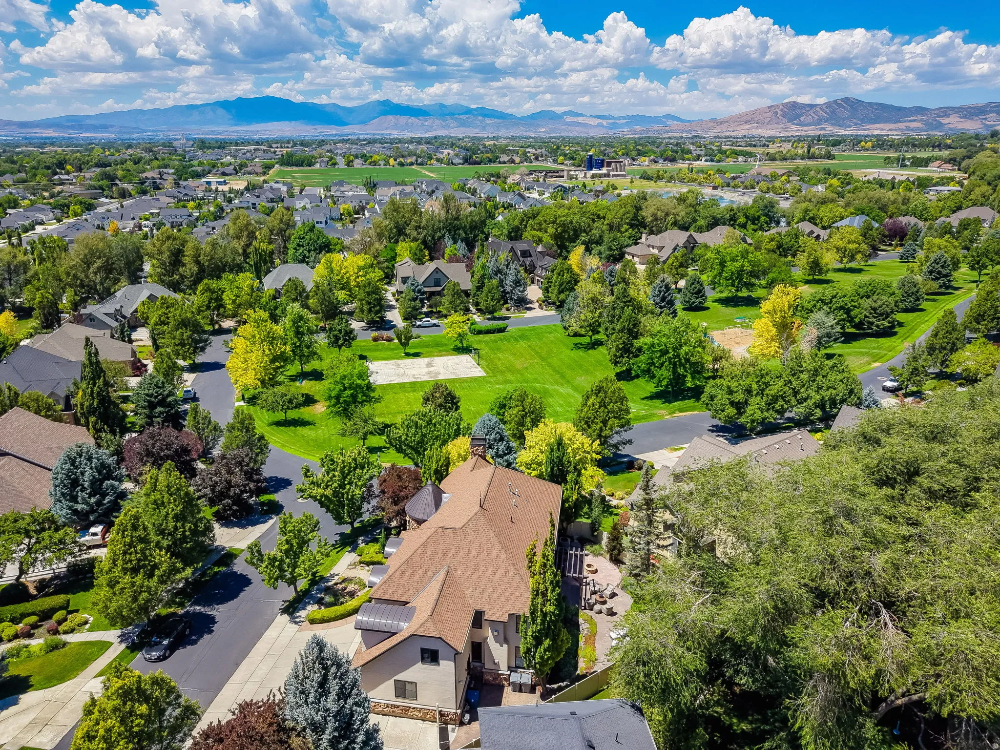 Expansive residential setting with varied architecture, mature trees, green spaces, paved roadways, and distant mountain scenery