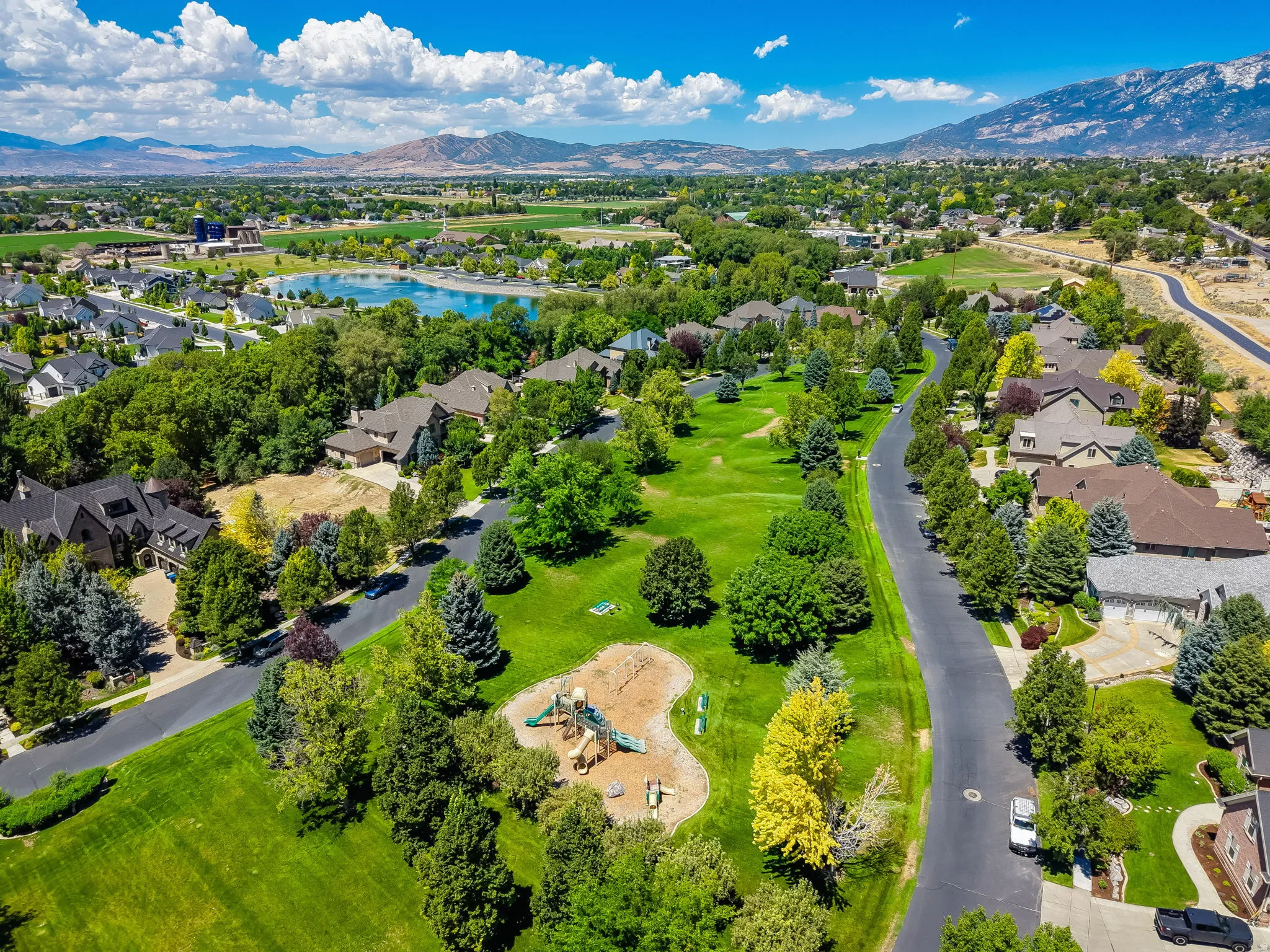 Lush green landscaping and mature trees surround a residential street with homes featuring varied architectural styles