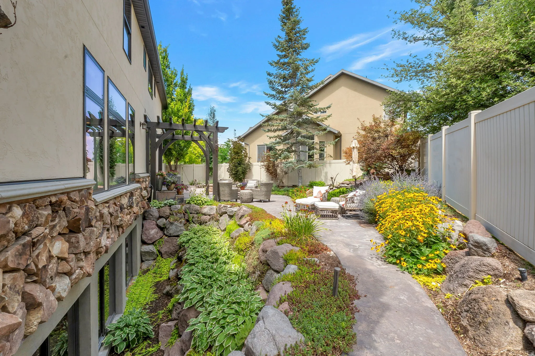Landscaped backyard featuring a stone pathway, mature plantings, and a white privacy fence