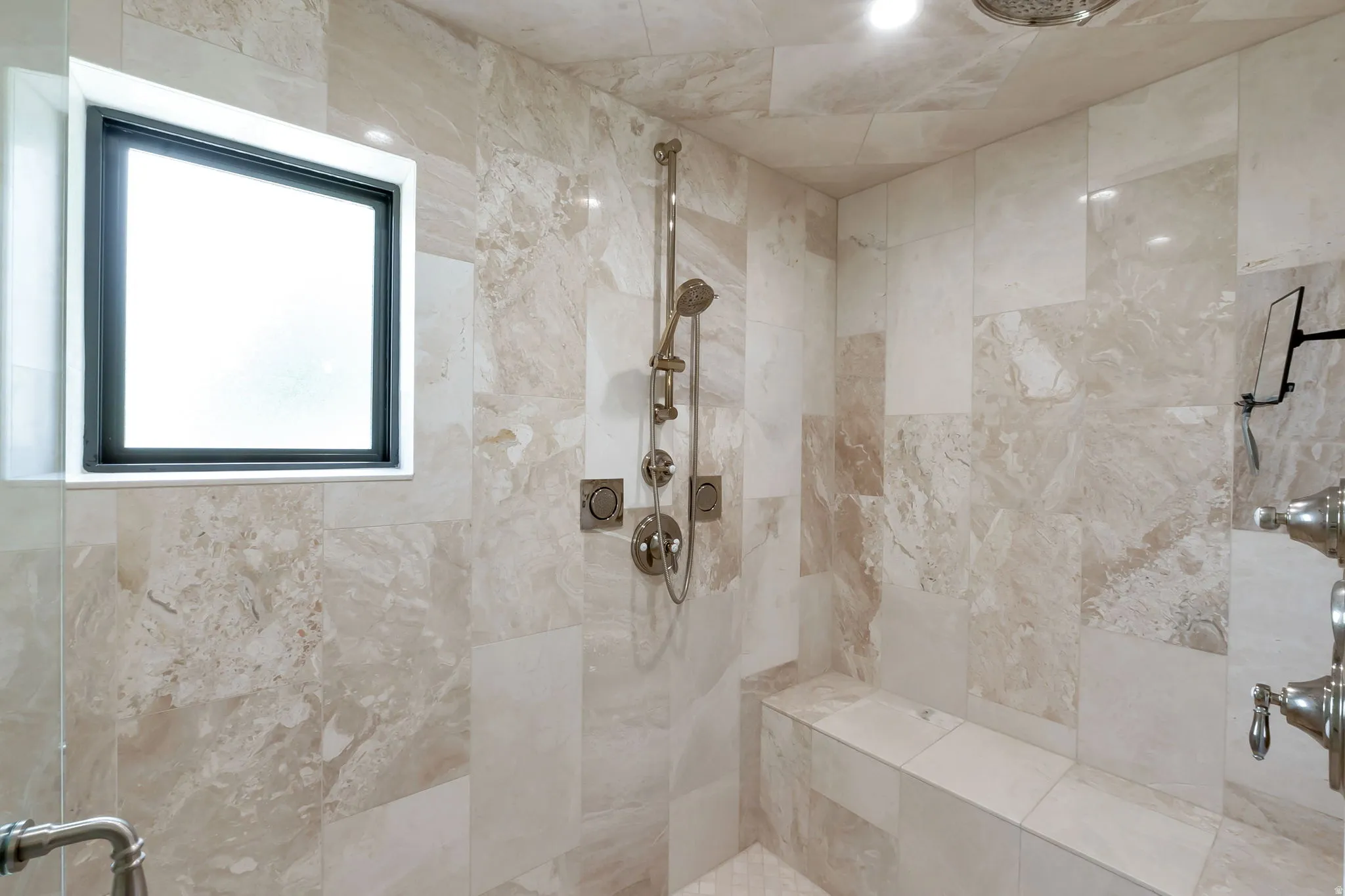 Shower with large format stone-look tile walls, built-in bench, and a multi-function shower system with a rainfall showerhead
