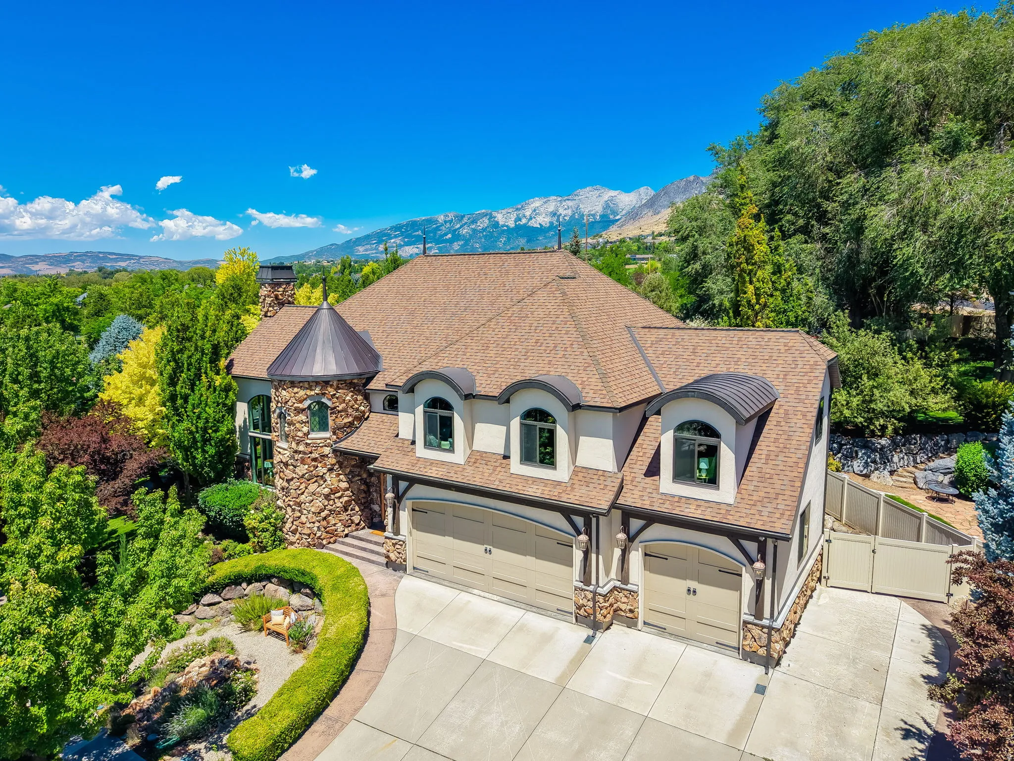 Stone and stucco exterior featuring a turret, dormer windows, a multi-car garage, and a concrete driveway